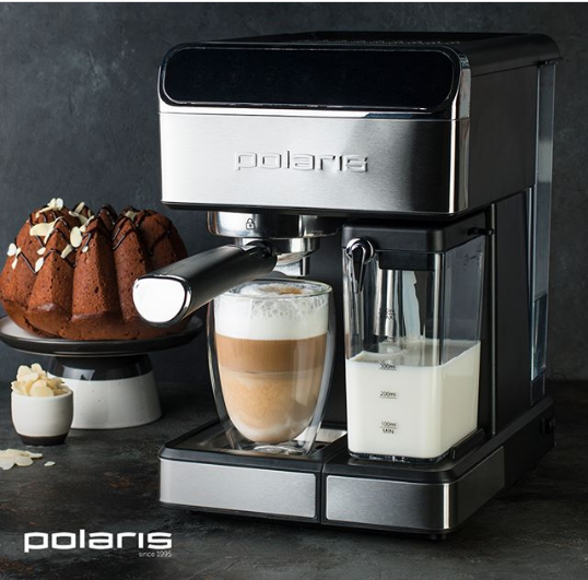 Черно-серая рожковая кофеварка Polaris со стаканом латте стоит на столе рядом с шоколадным кексом