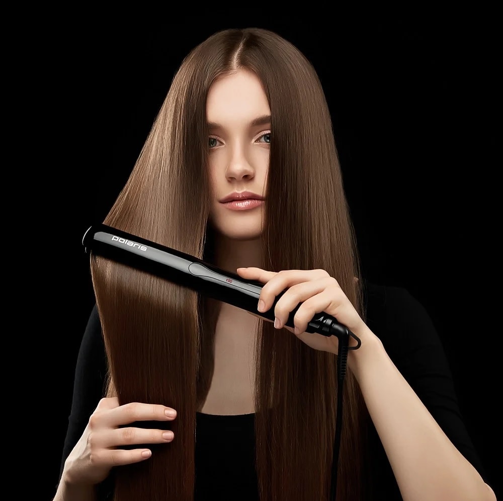 Молодая шатенка с длинными волосами использует стайлер Polaris PHSS 2595TAi Argan Therapy PRO