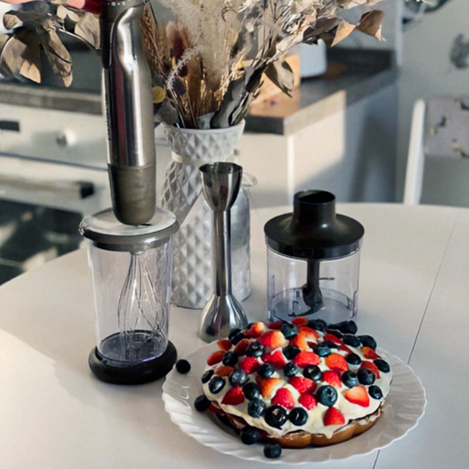 Погружной блендер Polaris вместе с насадками и ягодным пирогом стоит на столе