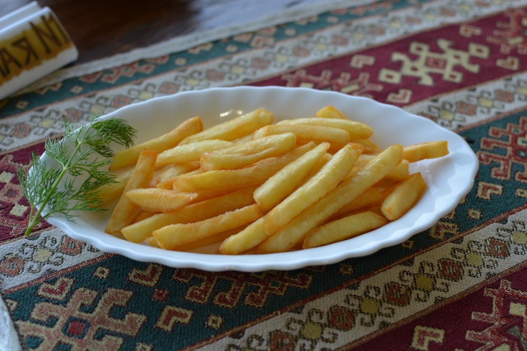 Картофель фри подан на белой тарелке с веточкой укропа